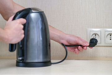 The man holds the electric power in his hand and connects the kettle to the outlet.