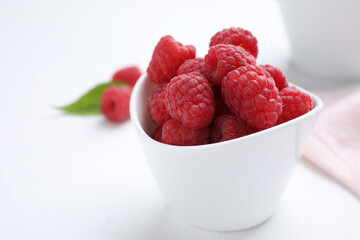 Delicious fresh ripe raspberries in bowl on white table, closeup