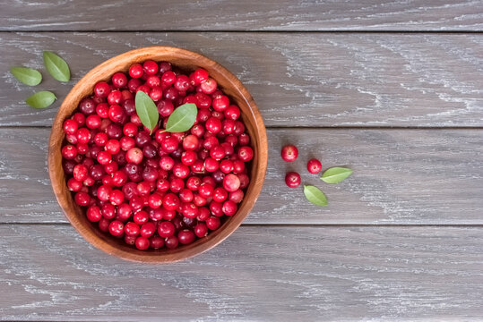 ripe cranberries in a wooden bowl on a wooden background top view. background with wild cranberries. copy of the space. the cranberries lay flat in the bowl.