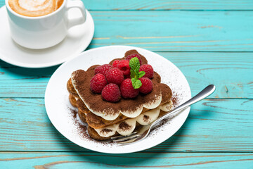 portion of Classic tiramisu dessert with raspberries and cup of espresso coffee on blue wooden background