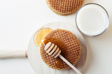 Honey dipper pouring honey over a pile of waffles on a wooden tray.