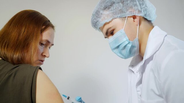 A nurse gives an intramuscular injection to a woman's shoulder.