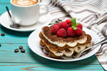 portion of Classic tiramisu dessert with raspberries and cup of espresso coffee on blue wooden background