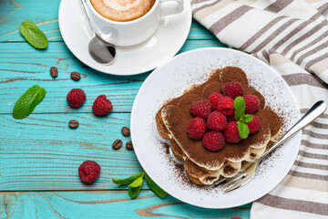 portion of Classic tiramisu dessert with raspberries and cup of espresso coffee on blue wooden background
