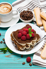 portion of Classic tiramisu dessert with raspberries and cup of espresso coffee on blue wooden background