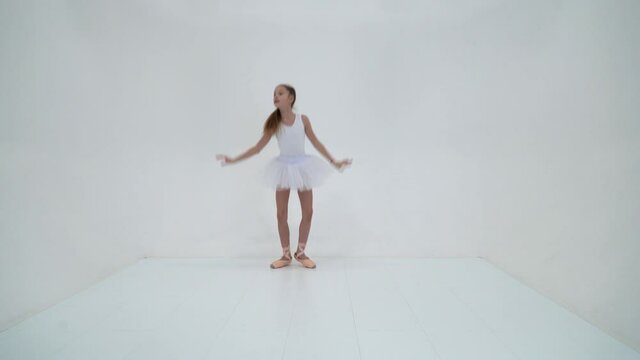 Cute little girl in a tutu and pointe shoes dancing in the studio on a white background.