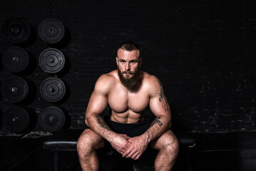 Fototapeta na wymiar Young strong sweaty muscular fit man with big muscles sitting in the gym taking a break after hardcore cross workout training