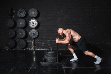 Young strong sweaty muscular fit man with big muscles pushing heavy weight plates on the prowler...