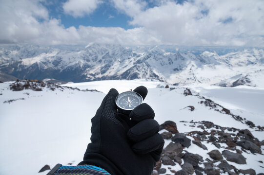 Magnetic compass in a man's hand in a glove against the background of the snow-capped mountains of the caucasus in the afternoon. Navigation concept