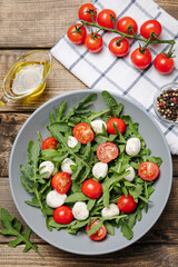 Diet and healthy salad with arugula, cherry tomatoes, mozzarella cheese and olive oil on wooden background