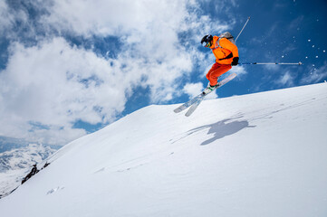 Man skier athlete makes a jump in flight on a snowy slope against the backdrop of a blue sky of...