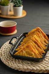 Easy recipe, snacks, minced pork meat filled fried wontons sort in black dish on weaving  placemat, grey placemat, brown wood table served with sweet plum sauce in red bowl