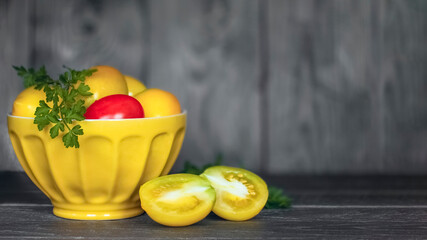 fresh yellow tomatoes in a yellow bowl on a wooden background close-up. background with fresh ripe tomatoes and a sprig of parsley. copy of the space.