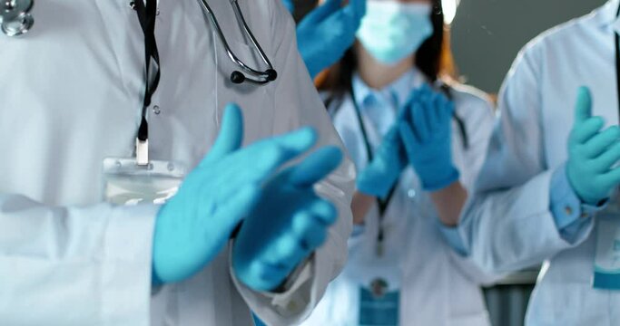 Close up of hands in blue rubber gloves applauding. Males and females doctors. in white medical gowns. Applause. Medics. Physicians colleagues. View from patient.
