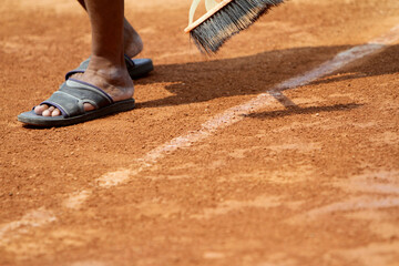 Field officers clean the clay tennis court lines with brooms before use