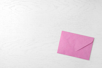 Pink paper envelope on white wooden background, top view. Space for text