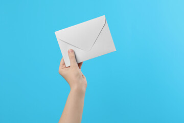 Woman holding white paper envelope on light blue background, closeup