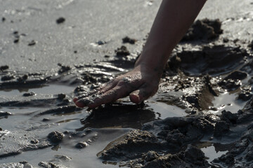 Silhouette of a child's hand playing in the mud or sand at the beach on a sunny day.