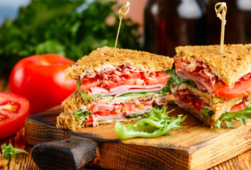 Delicious club sandwiches with green salad lettuce, ham, bacon, fresh tomatoes and sauce on a wooden cutting board. Lunch concept. Selective focus