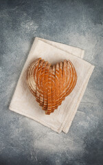 Sliced round loaf of rye bread in the shape of a heart on a gray linen napkin. Tasty and usefull home baking product close-up. Selective focus