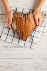 Sliced round loaf of rye bread in the shape of a heart on a  linen napkin in children's hands. Tasty and usefull home baking product close-up. Selective focus