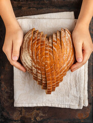 Sliced round loaf of rye bread in the shape of a heart on a gray linen napkin in children's hands....
