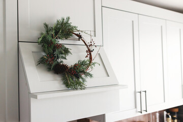 Rustic christmas wreath hanging on modern kitchen hood, festive holiday decoration.
