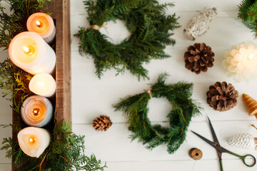 Candles and rustic christmas wreath with pine cones on white wooden table