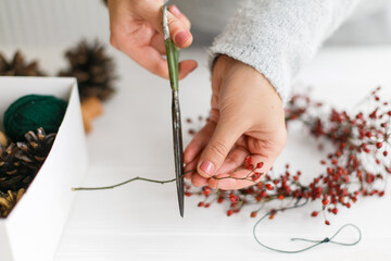 Female hands making simple christmas wreath with red berries