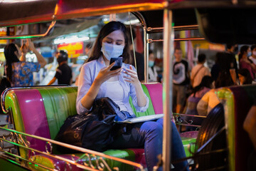 Traveler women wear the mask  using smartphone while ride on traditional thai taxi ,AKA tuk-tuk. Night time