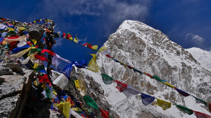 Colorful wind waving Buddhist prayer flags at trekking peak Kala Patthar (5,545 m) in Khumbu / Everest region, Himalaya, Nepal, with snow and ice covered mount Pumori in background and blue sky.
