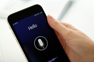 Woman using voice search on smartphone against blurred background, closeup