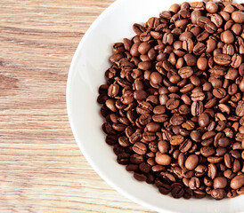 Coffee beans in a white bowl on a wooden background.