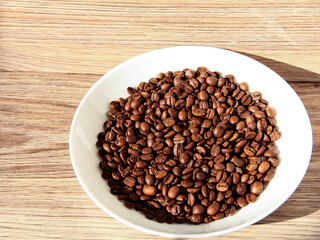 Coffee beans in a white bowl on a wooden background.