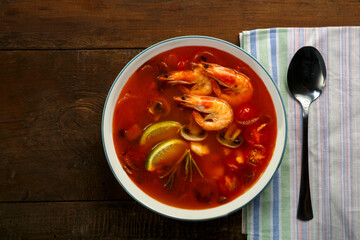 Tom yam soup with shrimp and lime in a plate next to a spoon on a napkin.