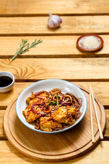 Soby with chicken and sesame seeds in teriyaki sauce on a wooden stand and sticks next to sesame seeds, herbs and soy sauce on a wooden table.