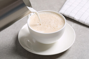 Pouring milk into cup of coffee on grey table