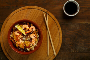 udon with mushrooms and shrimps in a clay plate on a round stand next to sticks.