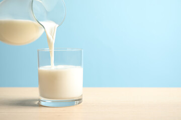 Pouring milk into glass on wooden table against light blue background. Space for text