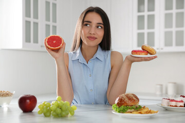 Woman choosing between grapefruit and doughnuts in kitchen