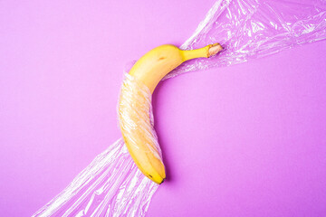Banana fruit wrapped in stretch wrap plastic on pink background, minimalistic creative layout, ecology and environment concept