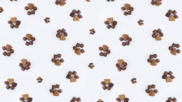 Minimalistic creative beautiful pattern of dry cat food in the shape of paws of different sizes on a white background.flat lay.The concept of proper nutrition for Pets.Pet store poster design