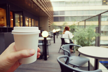 手に持った紙コップとカフェテラスの風景