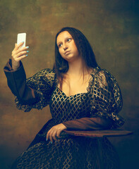 Selfie for gram. Young woman as Mona Lisa, La Gioconda isolated on dark green background. Retro style, comparison of eras concept. Beautiful female model like classic historical character, old