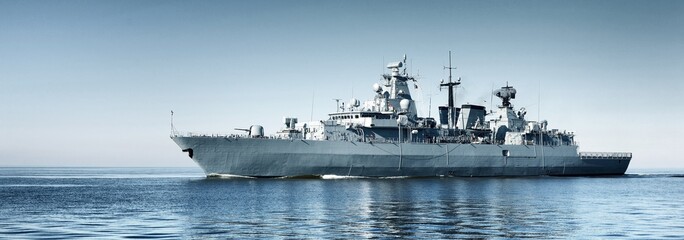Large grey modern warship sailing in still water. Clear blue sky. Baltic sea, Germany. Global...