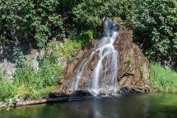 An artificial waterfall flowing down a rock into a reservoir. There are green trees around.