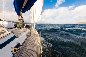 Sloop rigged modern yacht with wooden teak deck sailing near the rocky shore of the Firth of Clyde...