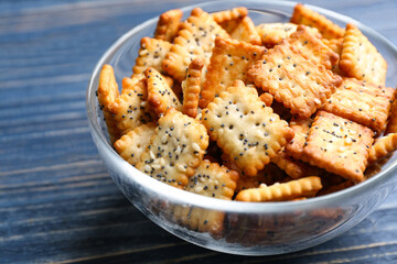 Delicious crispy crackers in bowl on blue wooden table, closeup