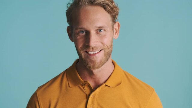 Young friendly blond bearded man confidently posing on camera and smiling over colorful background