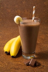 
Chocolate banana smoothie in a glass with ingredients on a brown background. Selected focus.
- 378830128